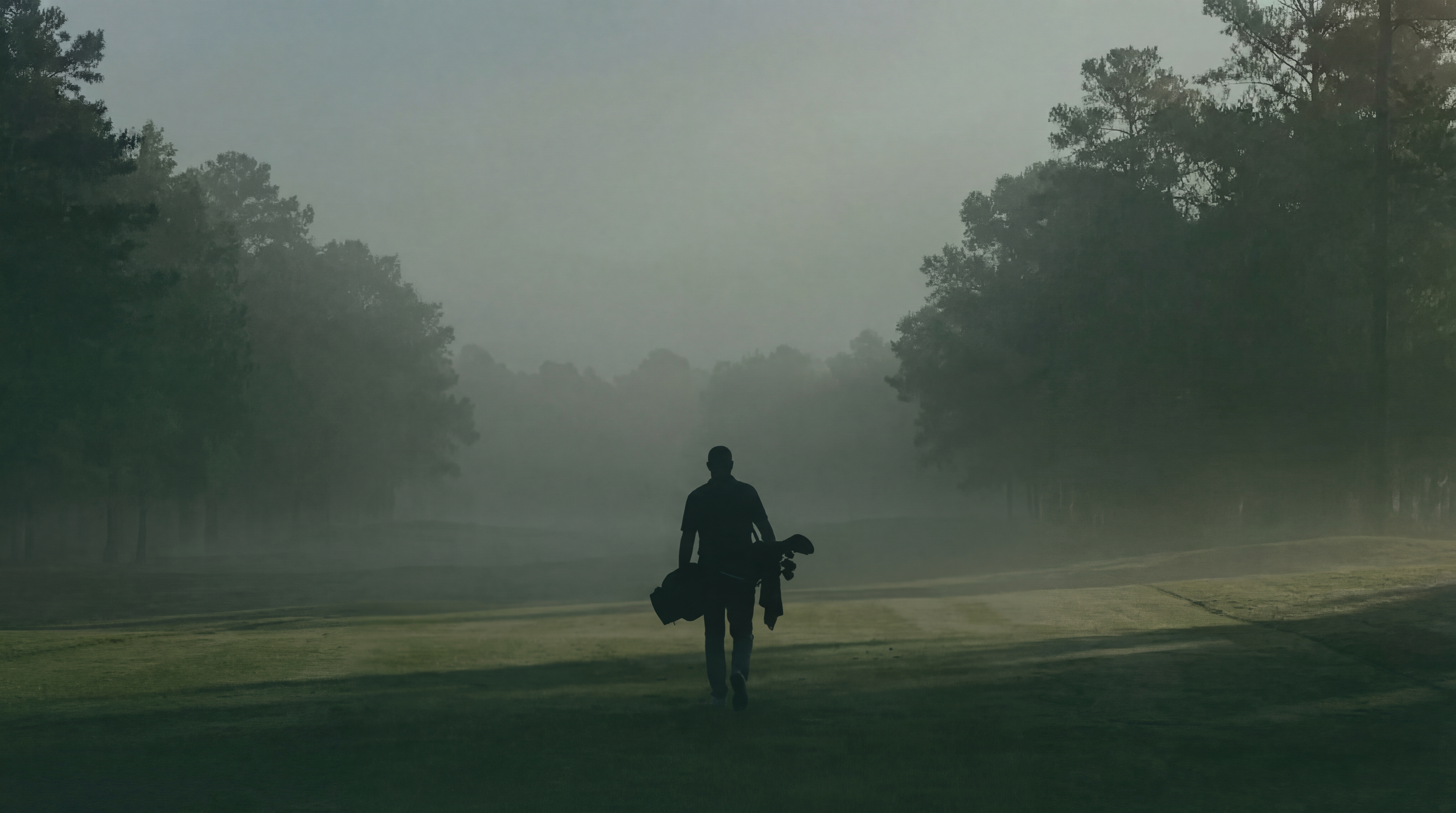 Golfer walking into morning mist at dawn